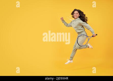 felice salto energico bambino con racchetta da tennis che corre al successo, copy space, vendita shopping sportivo. Foto Stock