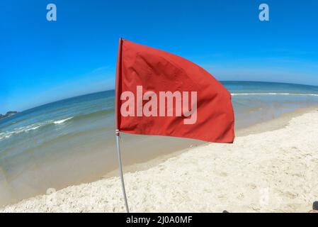 bandiera rossa sulla spiaggia che indica la zona di pericolo per il nuoto, in un cielo blu Foto Stock