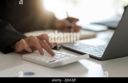Primo piano contabile che lavora alla scrivania in ufficio utilizzando la calcolatrice per calcolare il budget, prendendo nota del blocco note. Concetto di finanza e contabilità Foto Stock