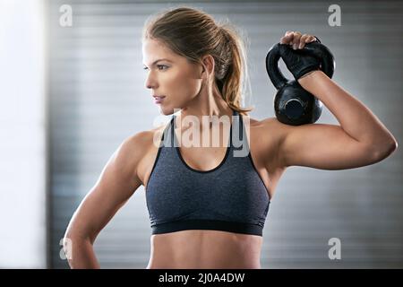 Costruendo la sua forza superiore del corpo. Shot di una giovane donna che si allenava con un campanello del bollitore in palestra. Foto Stock