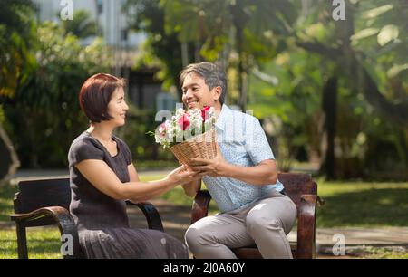 L'uomo di mezza età asiatico dà una rosa alla moglie in giorno di San Valentino Foto Stock