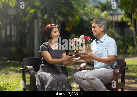 L'uomo di mezza età asiatico dà una rosa alla moglie in giorno di San Valentino Foto Stock