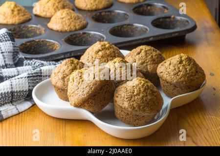 Muffin fatti in casa appena sfornati su un piatto da portata bianco e una teglia da forno sul tavolo da cucina. Gustosa colazione dolce, torte fatte in casa. Foto Stock