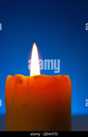 Primo piano di una candela che brucia contro il blu Foto Stock