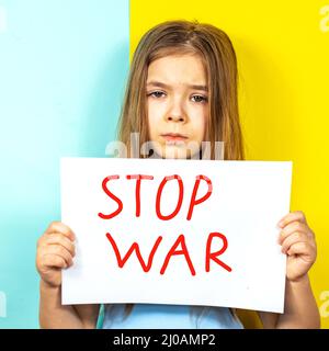 Una triste ragazza primo piano tiene un poster STOP WAR nelle sue mani sullo sfondo della bandiera Ucraina. Fermare la guerra in Ucraina. Il concetto di pace Foto Stock