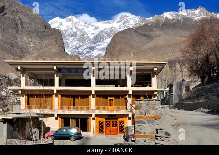 Picchi glaciali dietro l'edificio dell'hotel sulla città di Karimabad ad alta quota nella catena montuosa del Karakoram Foto Stock