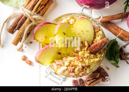 Fiocchi d'avena di mele pecan autunnali, porridge di avena con mele rosse, noci pecan e salsa al caramello, spazio copia di sfondo bianco in legno Foto Stock