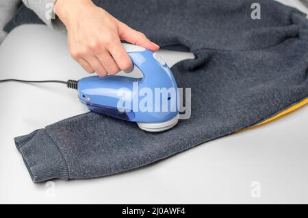 Macchina per la rimozione di pellet. Una donna rimuove i pellet dai pantaloni dei bambini con uno speciale dispositivo elettronico Foto Stock