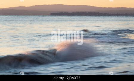 Le onde dell'oceano si infrangono sulla spiaggia di sabbia all'alba Foto Stock