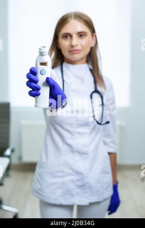 Una giovane dottore femmina misura la sua temperatura con un termometro elettronico senza contatto. Donna esaminata da un medico Foto Stock
