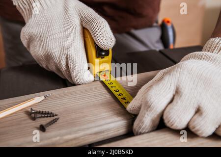 Il carpentiere misura la lunghezza delle assi o dei legnami misurando il nastro o il righello. Area di lavoro carpentiere, imprenditore artigiano. Primo piano della mano maschile Foto Stock