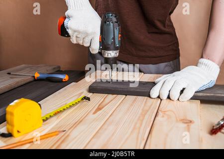 Primo piano ritratto e dettagli di lavoratore caucasico maschio utilizzando strumento cacciavite elettrico in mano e riparazione di nuovo scrivania in legno, miglioramento casa c Foto Stock