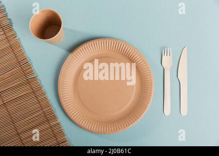 Utensili monouso ecologici realizzati in legno di bambù e carta su sfondo blu chiaro. Piastre, forcelle, coltelli, bicchieri di carta Foto Stock