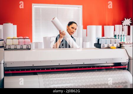 Giovane tecnico donna che lavora su plotter e taglierina per la stampa centar Foto Stock