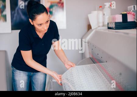 Giovane tecnico donna che lavora su plotter e taglierina per la stampa centar Foto Stock