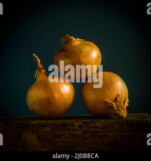 Tre cipolle marroni impilate su una superficie di legno su uno sfondo scuro Foto Stock