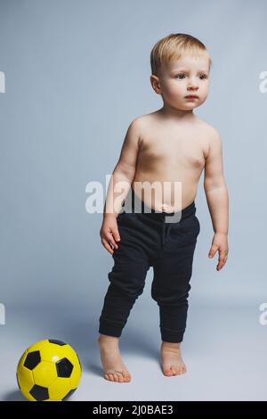 Fan boy che tiene in mano una palla da calcio, isolato su sfondo bianco. Newbie nel calcio, sport per bambini. Piccolo atleta. Foto Stock