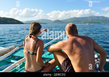 Donna e uomo seduto di fronte ad un filippino in legno barca tradizionale guardando il mare blu Foto Stock