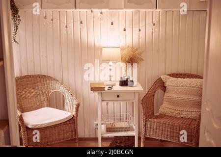 Interni in stile bohémien con un'accogliente atmosfera serale. Casa accogliente, confortevole con arredamento a secco canne, vecchia macchina fotografica, libro vintage e lampada da tavolo. Interno estetico Foto Stock