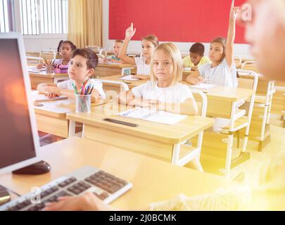 Vista dall'insegnante di alunni della scuola elementare che alzano le mani Foto Stock