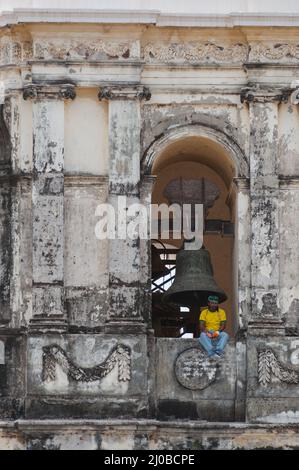 L uomo indossa maglietta gialla seduti sulla battuta del top ol una chiesa con tetto bianco Foto Stock