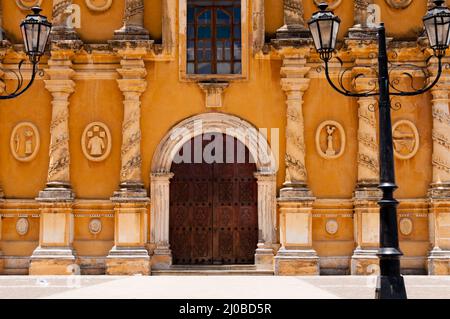 Vecchia laterna di fronte chiesa gialla con marrone grande porta di legno, pietra scarving e finestra in vetro Foto Stock