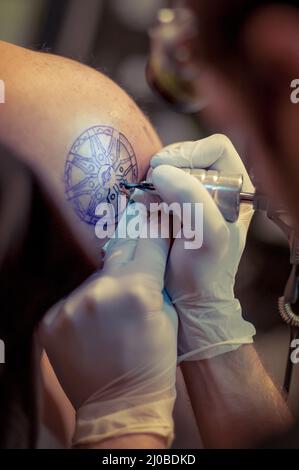 Master tatuaggio disegna la vernice blu sul tatuaggio del cliente Foto Stock
