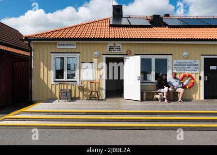 Oregrund, Uppland / Svezia - 30 07 2019: Facciata e due anziani seduti di fronte a un vecchio ufficio portuale o hannkontoret per il controllo delle frontiere Foto Stock