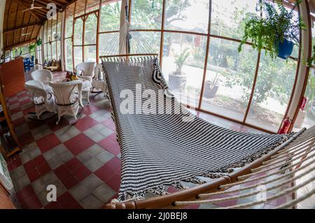 Bianco amaca enorme e arredi in rattan sul pavimento piastrellato in ostello Foto Stock