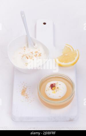 Gelatina di limone con crema e marmellata in un bicchiere su una tavola bianca Foto Stock