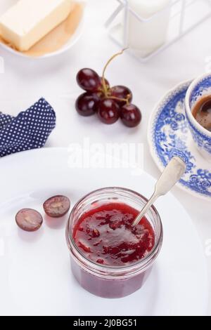 Marmellata di uva rossa in un vaso di vetro su uno sfondo bianco Foto Stock