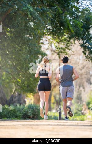Vista posteriore della giovane coppia che fa sport che corre su un sentiero del parco Foto Stock
