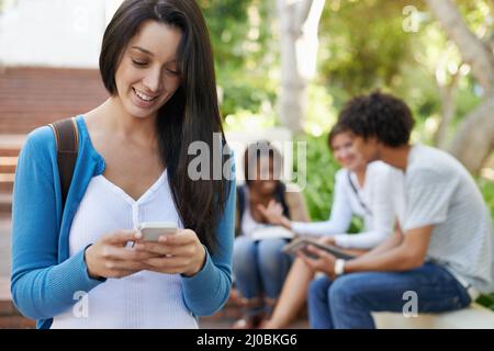 Soggiorno dopo classe a study...see più tardi. Vista ritagliata di una studentessa universitaria femminile che usa il suo telefono mentre si trova nel campus. Foto Stock