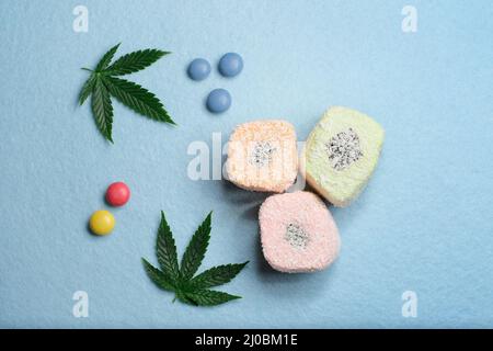 Foglie di marijuana verde su sfondo blu testurizzato. Dessert di cannabis. Delizia turca con fiocchi di cocco e confetti di caramelle colorate, vista dall'alto. Laou Foto Stock