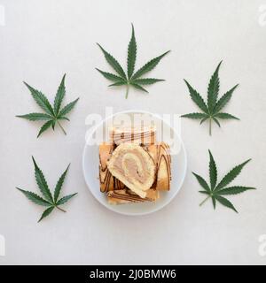 Rotolo dolce con olio di marijuana su piatto bianco. Cucina di cannabis. Disposizione dei deliziosi dessert, vista dall'alto da vicino. Foto Stock