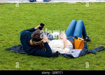 Inghilterra, Londra, Southwark, Potters Field Park, coppia che giace su Grass guardando gli smartphone Foto Stock