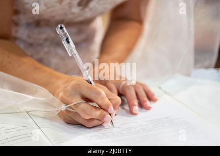 Marzo 2022, la mano della giovane sposa firma il registro del matrimonio Foto Stock