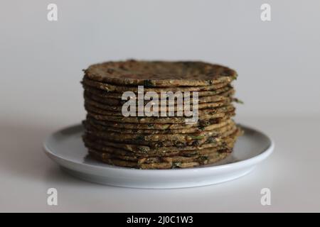 Bajra methepla. Pane piatto indiano fatto di farina di miglio di perla, foglie di fieno, semi di sesamo, yogurt e spezie. Scatto su sfondo bianco. Foto Stock