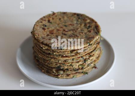 Bajra methepla. Pane piatto indiano fatto di farina di miglio di perla, foglie di fieno, semi di sesamo, yogurt e spezie. Scatto su sfondo bianco. Foto Stock