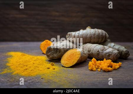 Curcuma, spezia asiatica sana come radici, polvere fresca grattugiata e secca contro legno rustico scuro, effetti antinfiammatori e antiossidanti e una forte y Foto Stock
