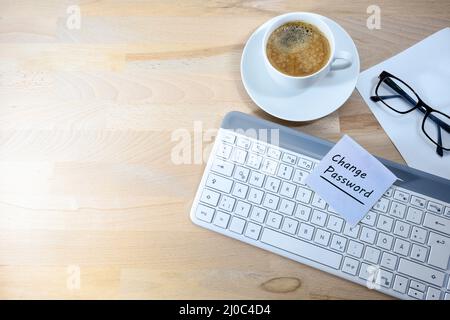 Cambia password, scritta su una nota adesiva su una tastiera di computer, scrivania in legno per ufficio con tazza di caffè, carta e bicchieri, concetto per la sicurezza dei dati in Foto Stock