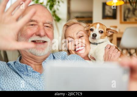 Coppia felice di anziani con il cane piccolo hanno video chat divertente con la famiglia a casa Foto Stock