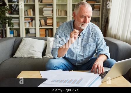 Uomo anziano pensivo che fa la contabilità o che lavora sulla dichiarazione di imposta sul computer portatile Foto Stock