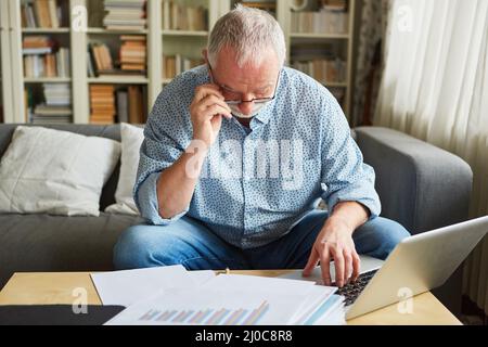 Vecchio al computer portatile che fa la contabilità o prepara la dichiarazione d'imposta Foto Stock