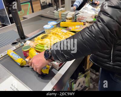 Karlsruhe, Germania - 12 marzo 2022: Vista laterale dell'uomo arrangiare più dolci alimentari conserve di frutta vegetale sul banco nel supermercato ipermercato - shopping di generi alimentari Foto Stock