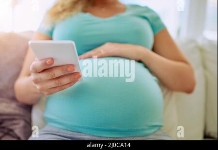 Mantenere tutti aggiornati con la sua gravidanza. Primo piano di una donna incinta testando sul suo cellulare a casa. Foto Stock