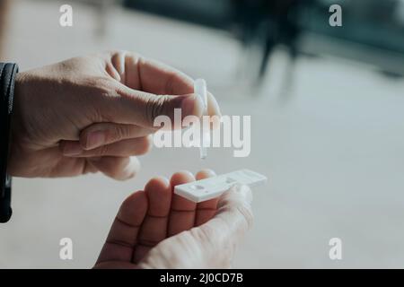 primo piano di un giovane uomo, per strada, mentre sta ponendo il suo campione nel dispositivo di test diagnostico dell'antigene covid-19 Foto Stock