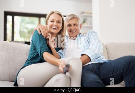 Sostituzione della stazione. Ritratto corto di una coppia matura affettuosa che guarda la televisione insieme a casa. Foto Stock