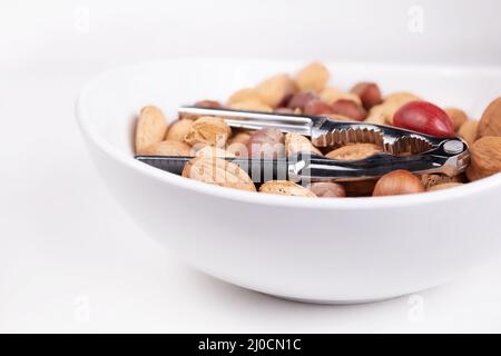 Varietà di dadi a guscio con pinze per dadi in un recipiente, primo piano. Mucchio di noci non salate, noci pecan, mandorle e nocciole in guscio. Conc. Grasso sano Foto Stock