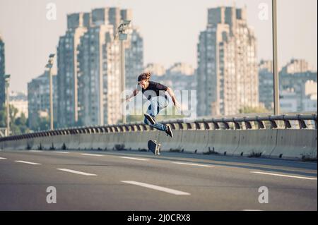 Skater fare trucchi e saltare sul ponte stradale, attraverso il traffico urbano. Skateboard a cavallo gratuito Foto Stock